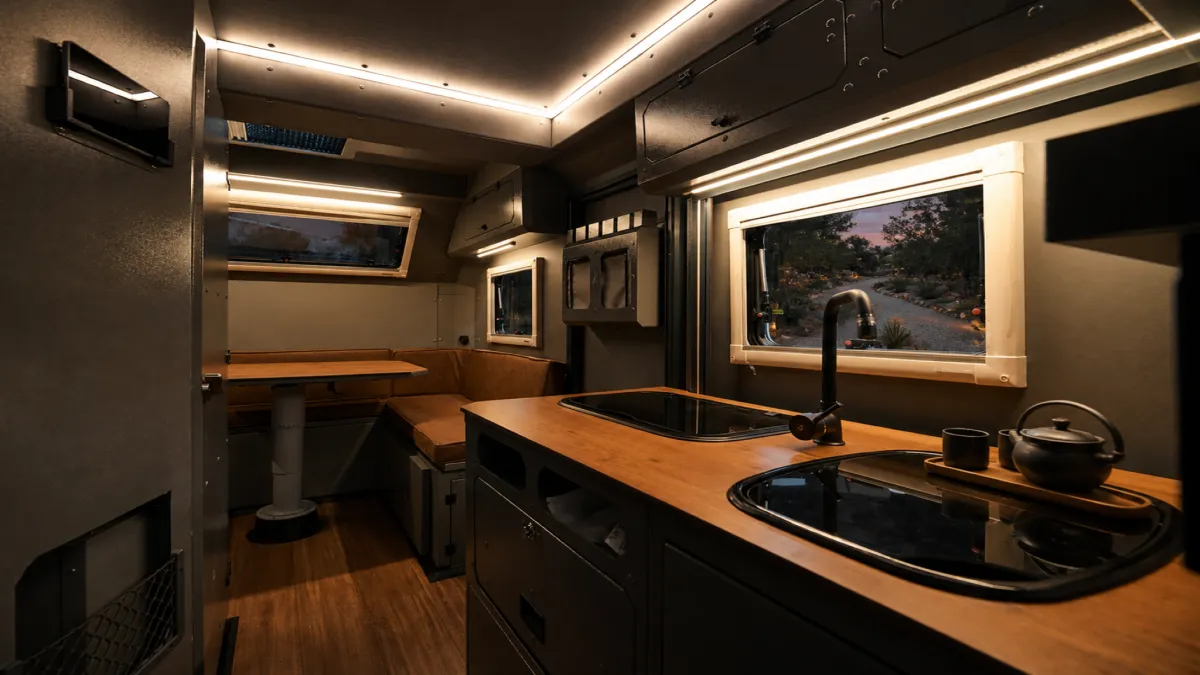 The kitchen of a caravan at dusk, a wooden worktop with a hob and a sink, the track through the window