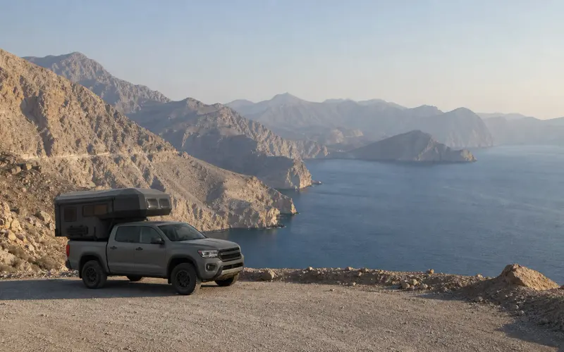 A pickup camper above mountains that drop into the sea