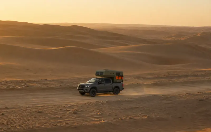 A pickup camper crossing the dunes at sunset