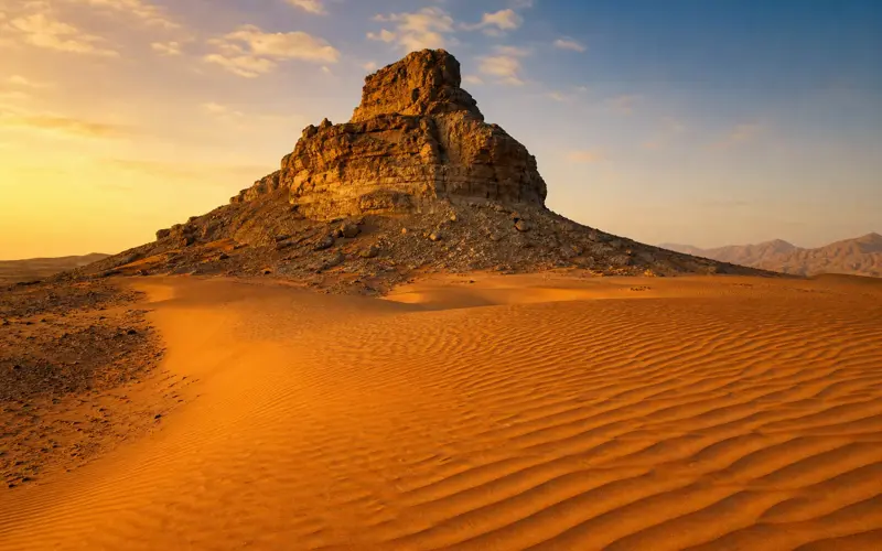 The rock of Fossil Rock rising over orange dunes